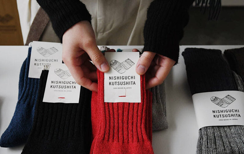 hands holding Nishiguchi Kutsushita socks with branded packaging