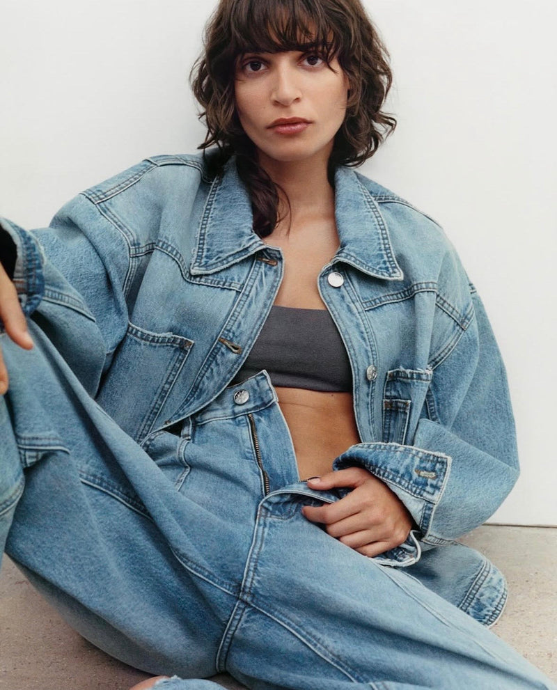 Person wearing jeans and a denim jacket sitting on the ground