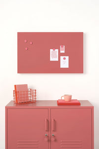 Pink magnetic display board above a pink locker with a white wall background