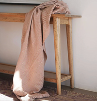 Patterned blanket draped over a wooden bench against a white wall.