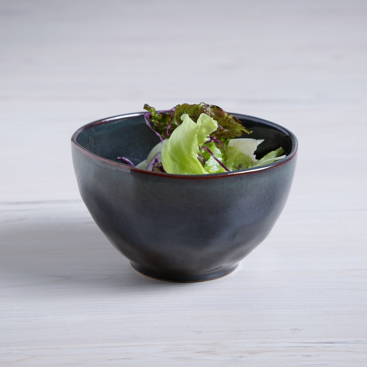 Dark blue ceramic bowl with green salad on a light wooden surface