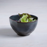 Dark blue ceramic bowl with green salad on a light wooden surface