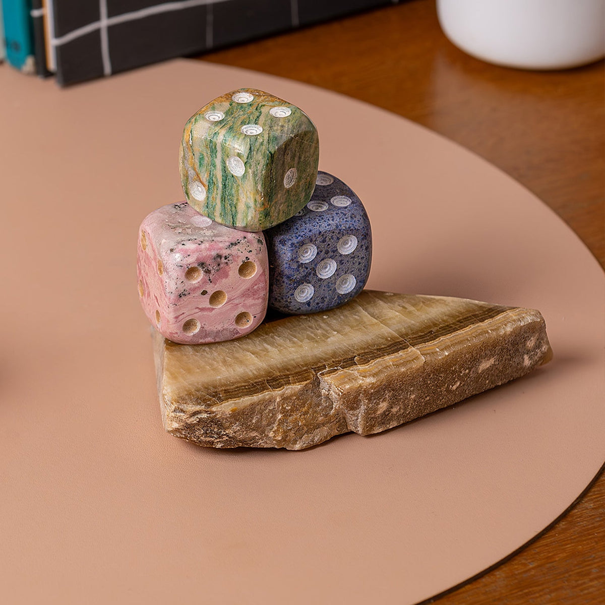 Three colorful stone dice stacked on a raw piece of onyx on a neutral table surface