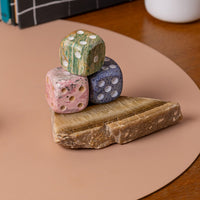 Three colorful stone dice stacked on a raw piece of onyx on a neutral table surface