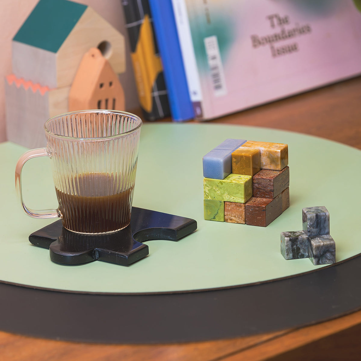 Clear glass mug with coffee, stone cube puzzle, and books on a green surface