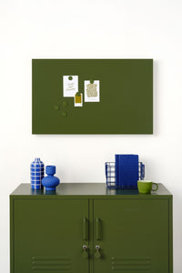 Green magnetic display board on a white wall above a green locker cabinet with decorative items.