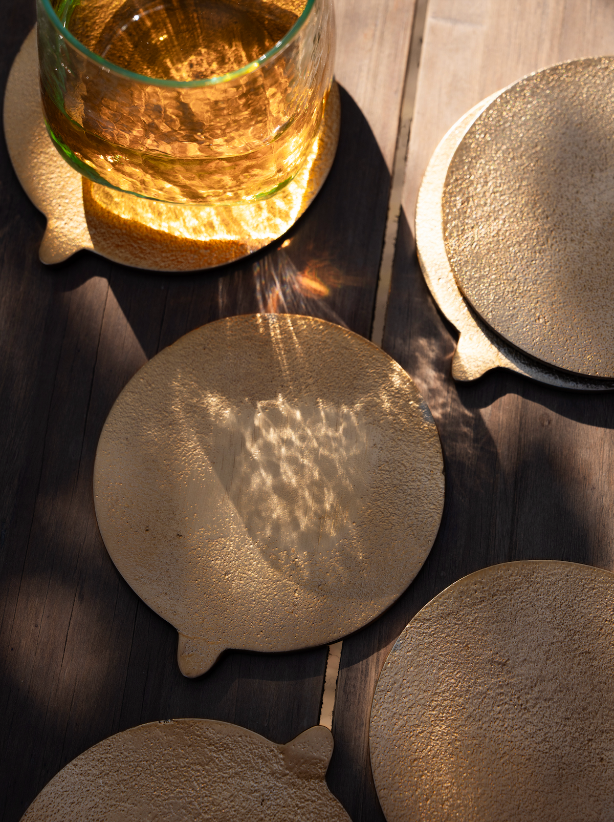 Round brass coasters on a wooden surface with a glass of amber liquid.