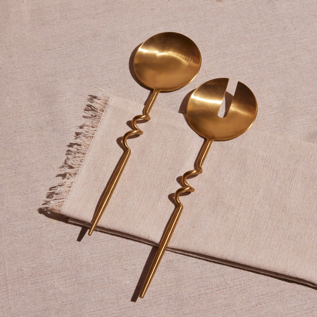 Pair of gold-colored serving spoons on a textured beige surface