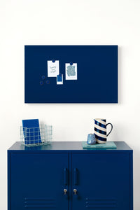 Navy blue magnetic display board on a white wall above a blue locker cabinet with decorative items.