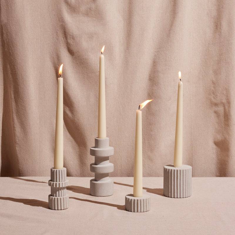 Four taper candles in decorative holders against a beige curtain background
