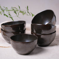 Set of black ceramic bowls on a light surface with a plant in the background
