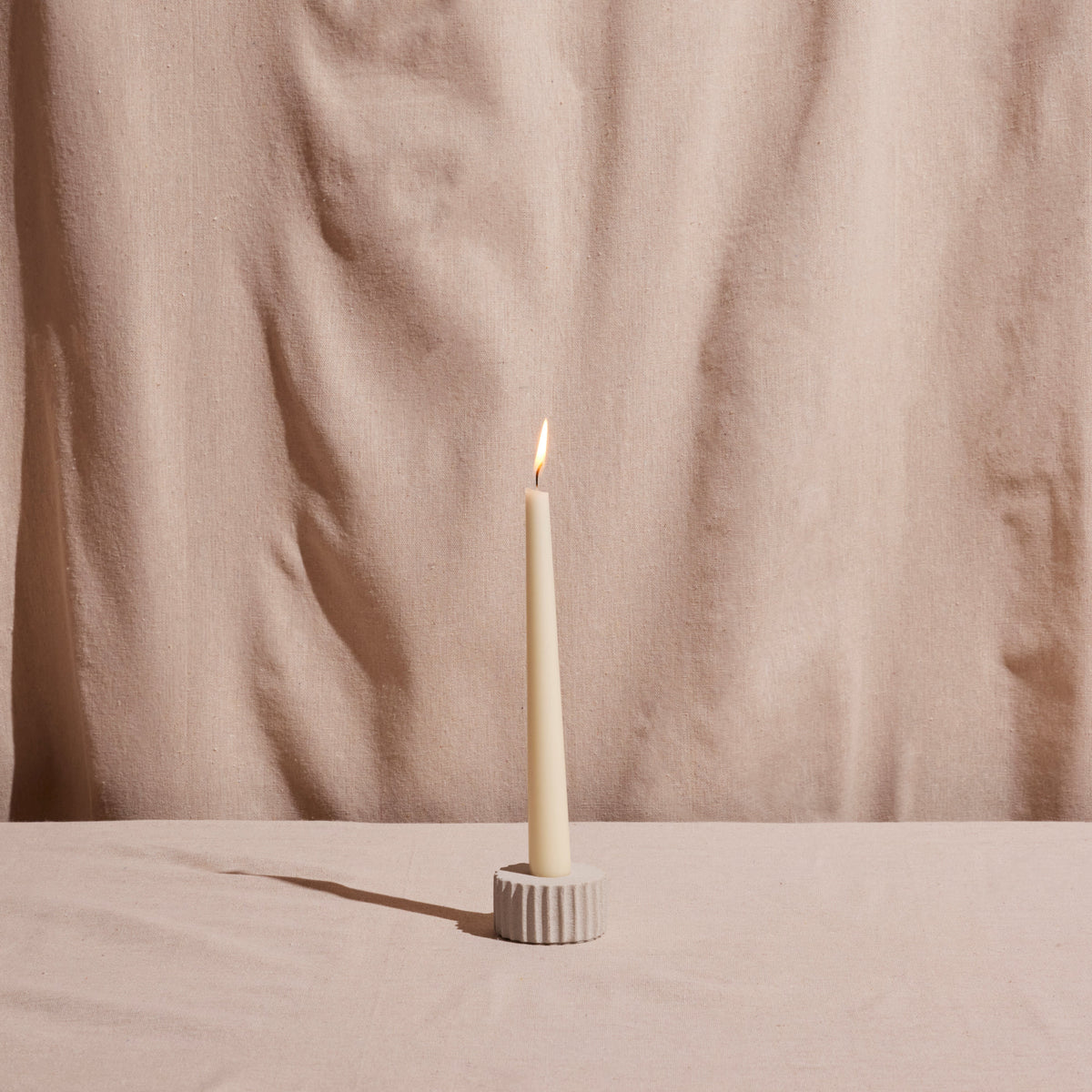 White candle in a holder on a beige surface with a beige curtain background