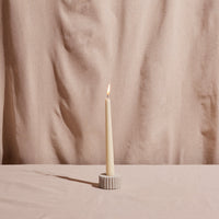 White candle in a holder on a beige surface with a beige curtain background