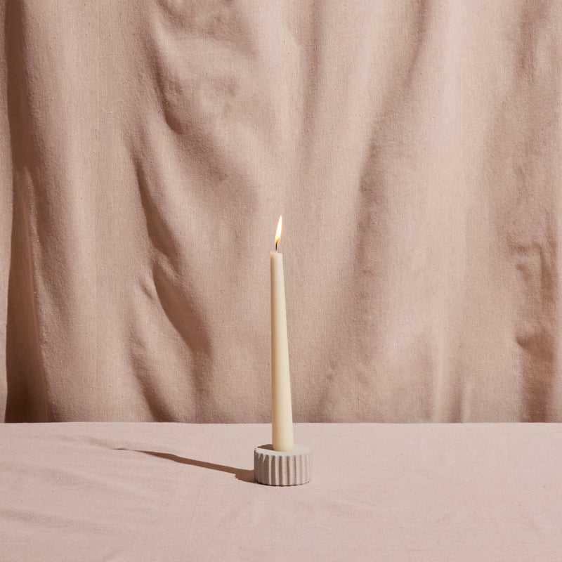White candle in a holder on a beige surface with a beige curtain background