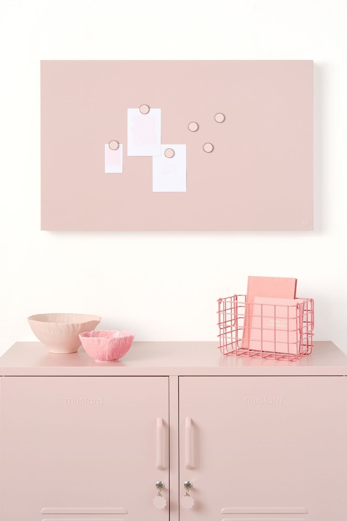Pink wall-mounted storyboard with magnetic items on a white cabinet