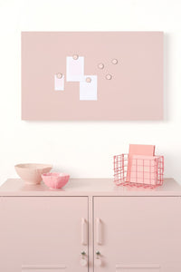 Pink wall-mounted storyboard with magnetic items on a white cabinet