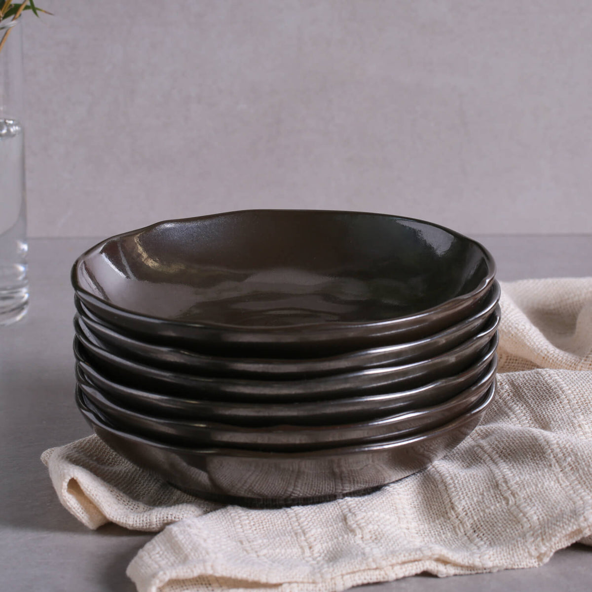 Stack of black metallic pasta plates on a light gray surface with a beige towel underneath.