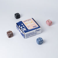 Four colorful stone dice arranged around a packaging box for giant dice on a white surface