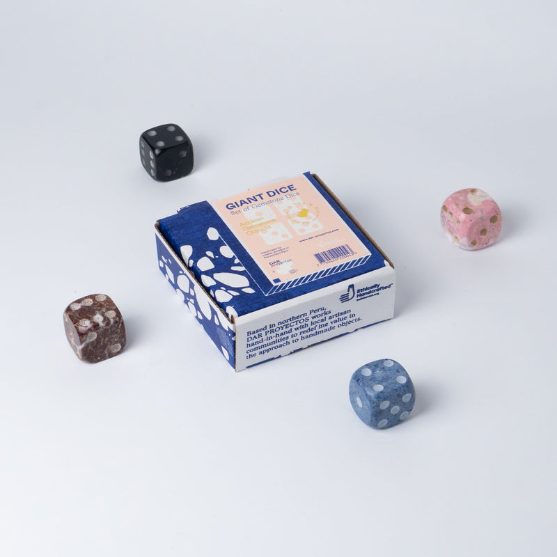 Four colorful stone dice arranged around a packaging box for giant dice on a white surface