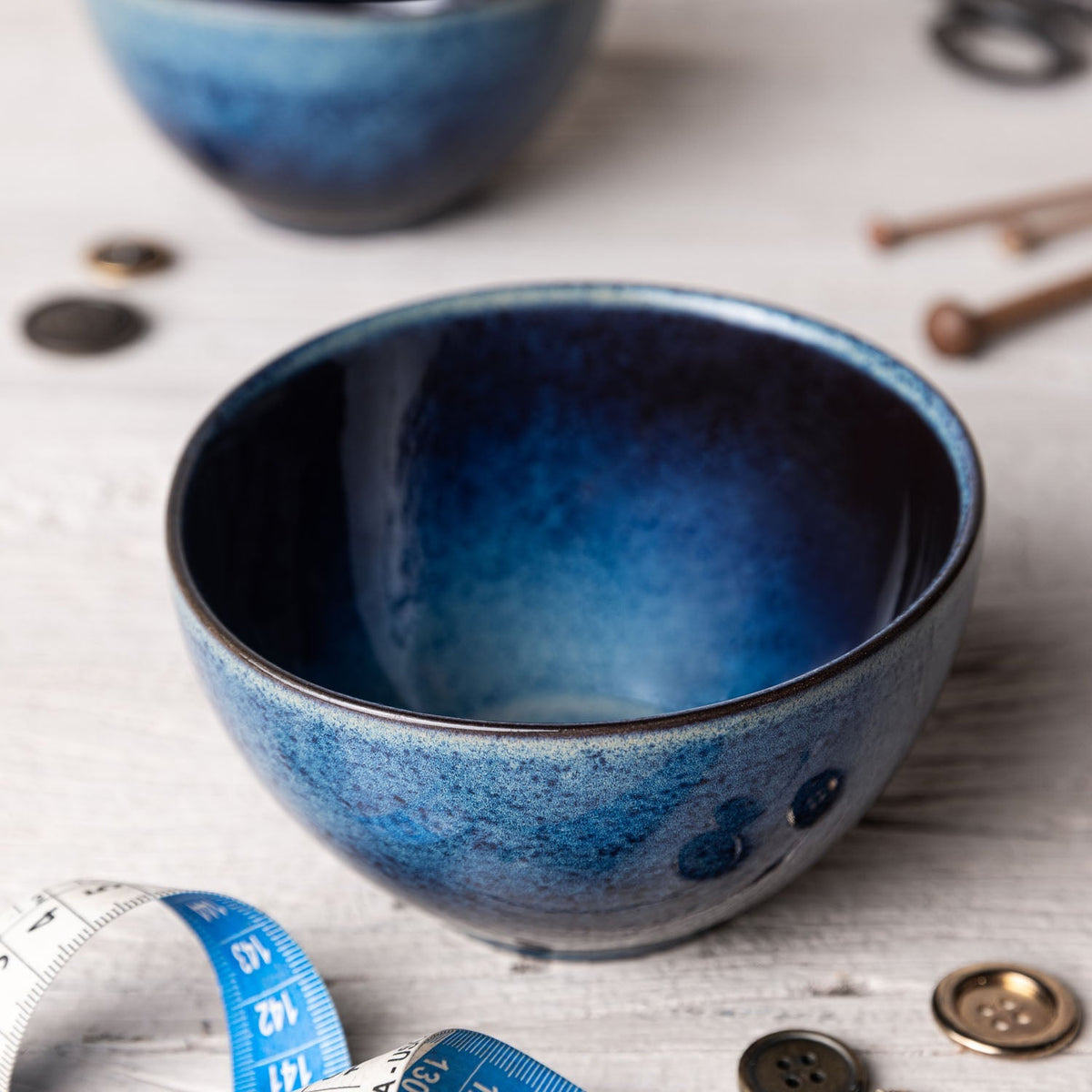Blue ceramic bowl on a textured surface with buttons and a measuring tape.