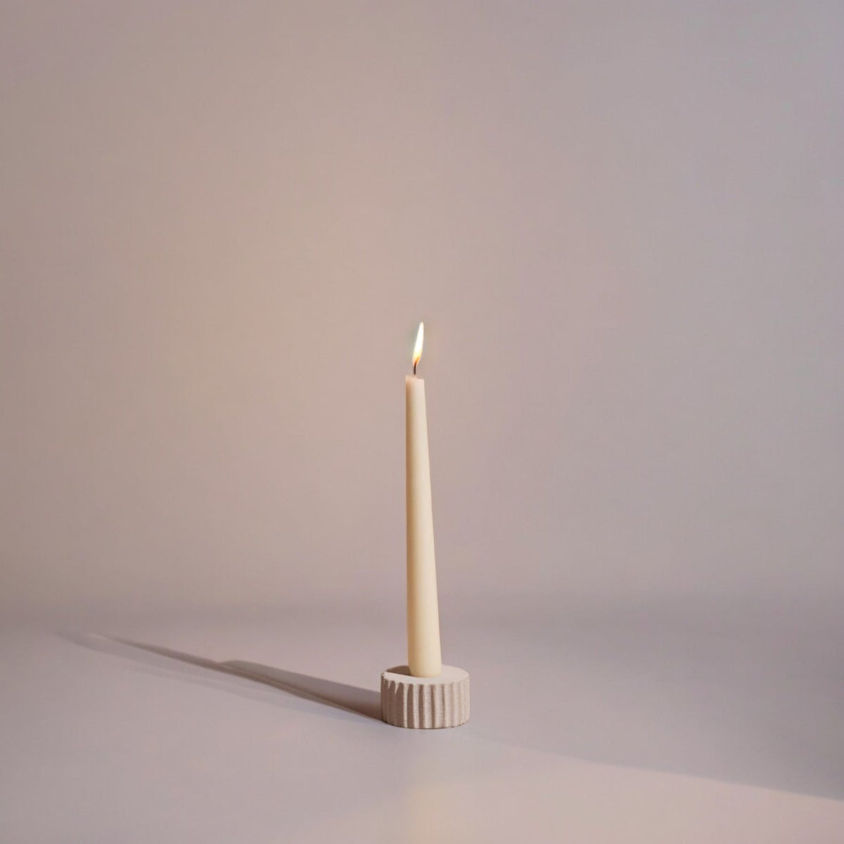 Taper candle in a decorative holder on a plain background