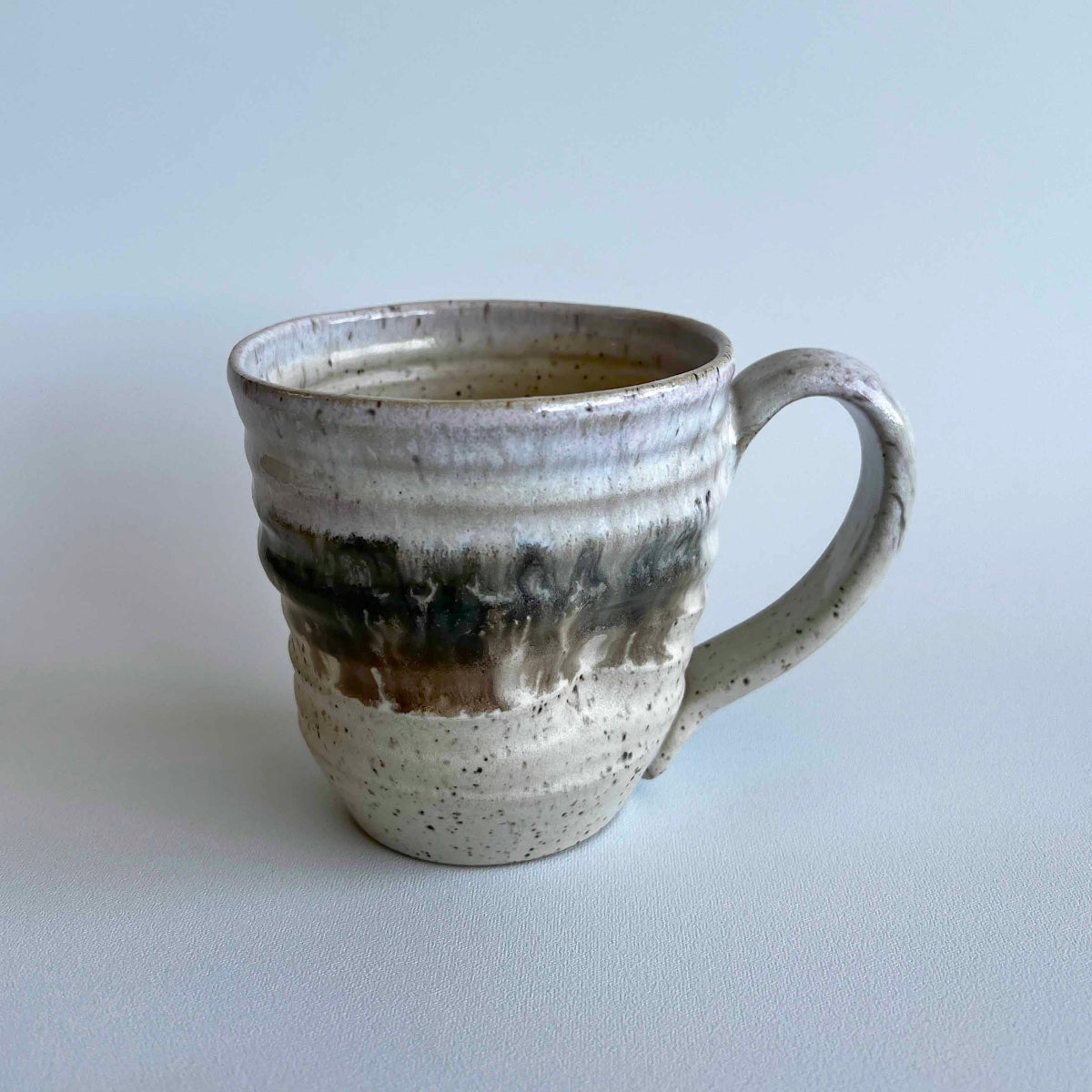 Ceramic mug with light and dark neutral glaze details on a white background