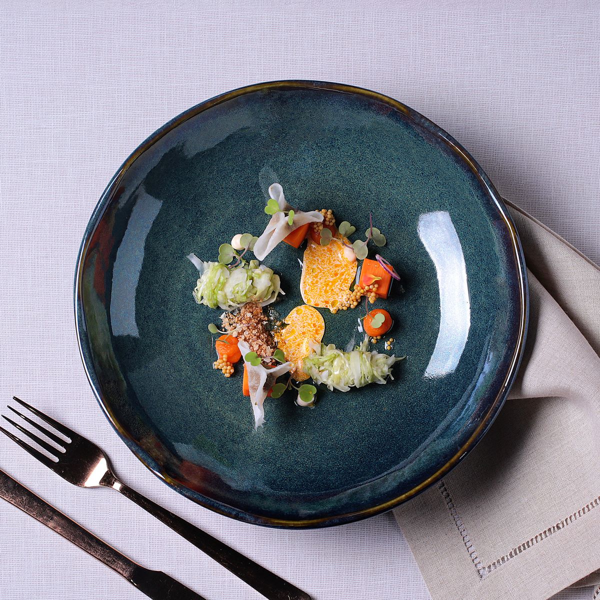 Blue ceramic plate with a gourmet dish of vegetables and a fork on a light gray background