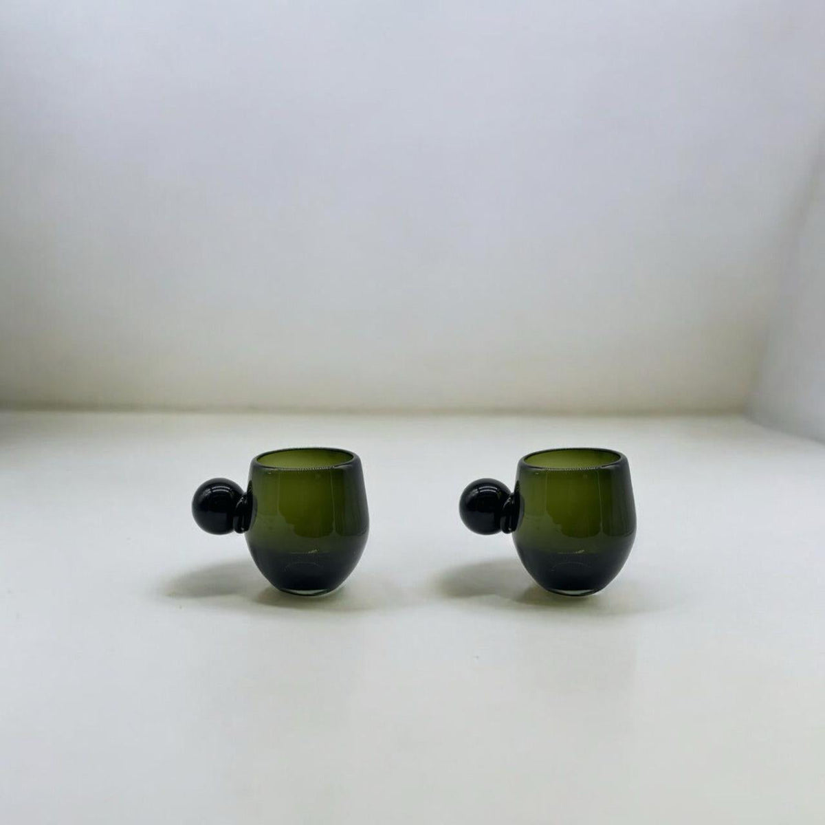 Two green glass cups with spherical handle accents on a white surface