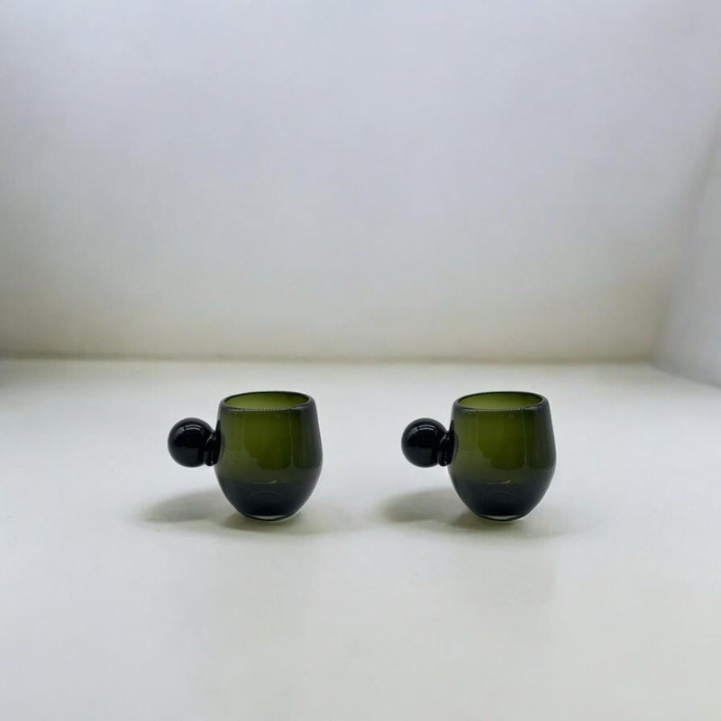 Two green glass cups with spherical handle accents on a white surface