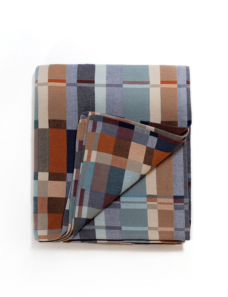 A folded plaid blanket with a multicolor pattern of blue, brown, beige, and gray blocks, shown on a clean white background.