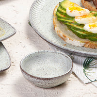 Speckled ceramic ramekin with a plate of avocado toast on a light surface.