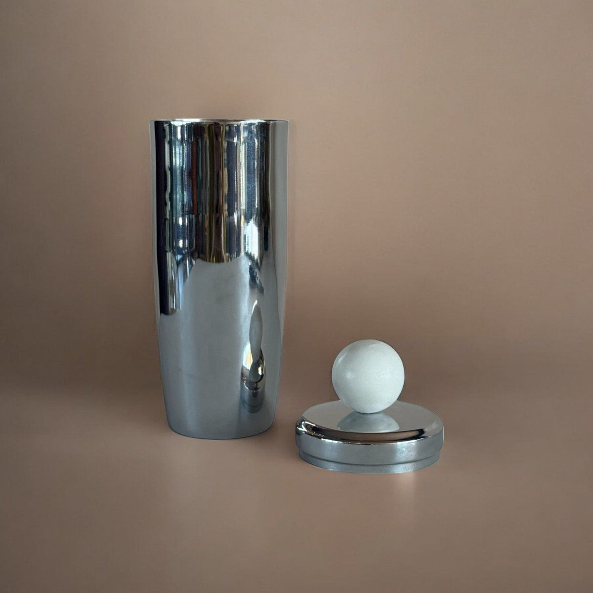 metal cocktail shaker with marble sphere on lid, lid removed on brown background