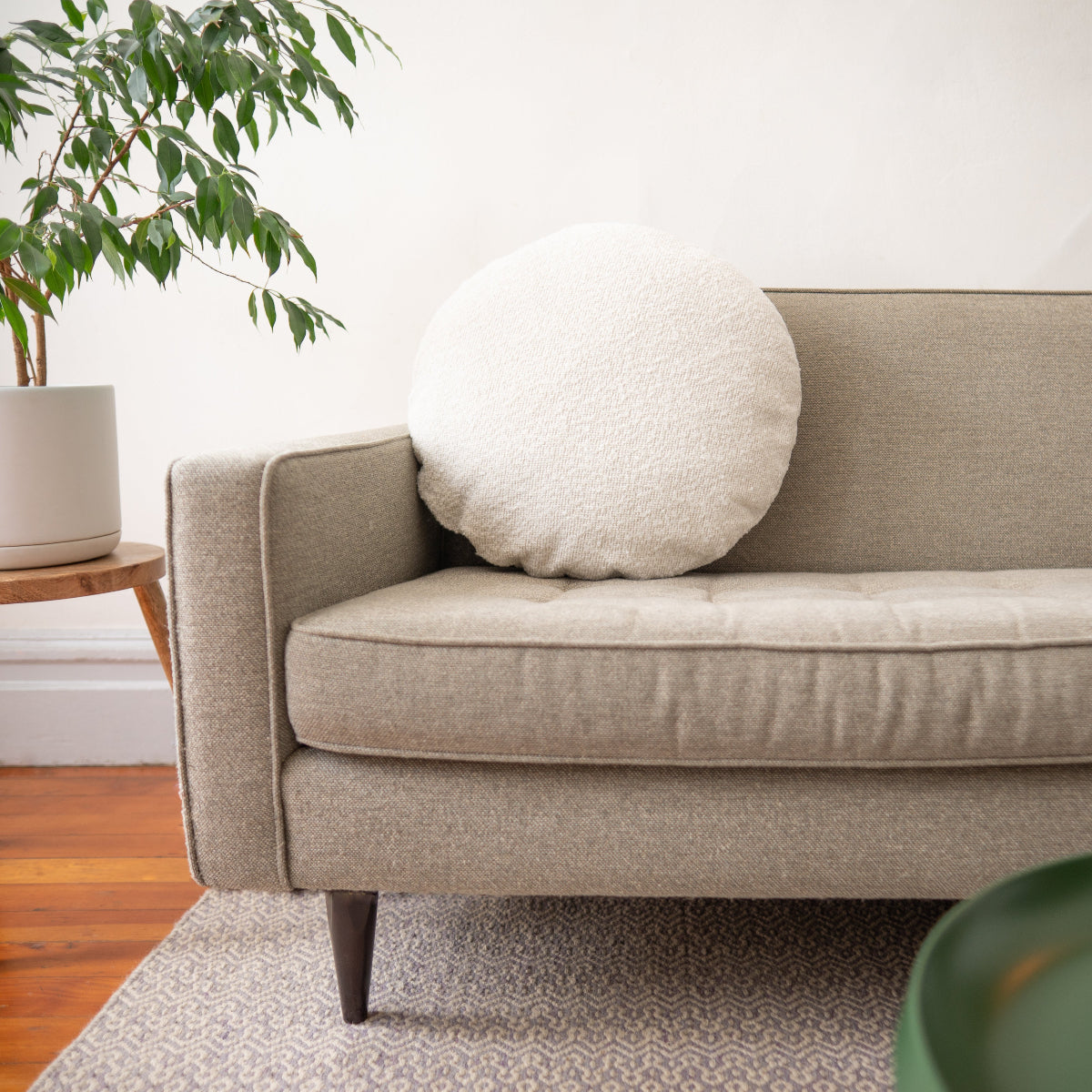 Beige sofa with a round pillow in a room with a plant and wooden floor.