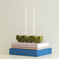 Green stone candle holder on top of books with two taper candles