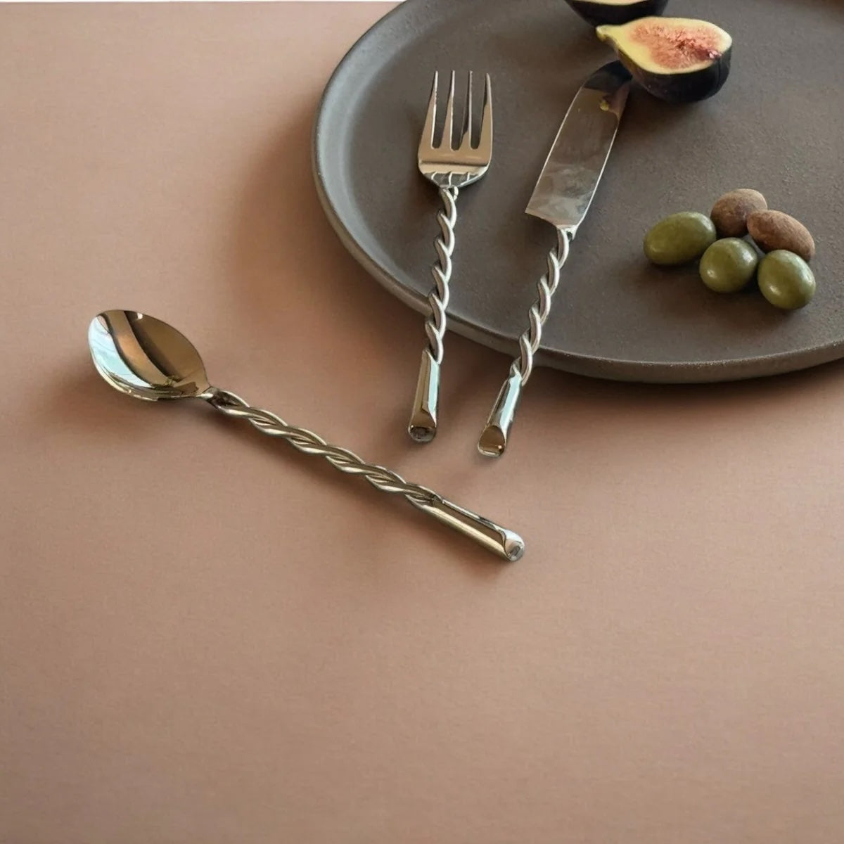 Silver cutlery set on a brown surface with a plate and fruits.