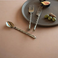 Silver cutlery set on a brown surface with a plate and fruits.