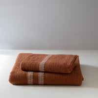 Folded rust color textured towels on a white surface 