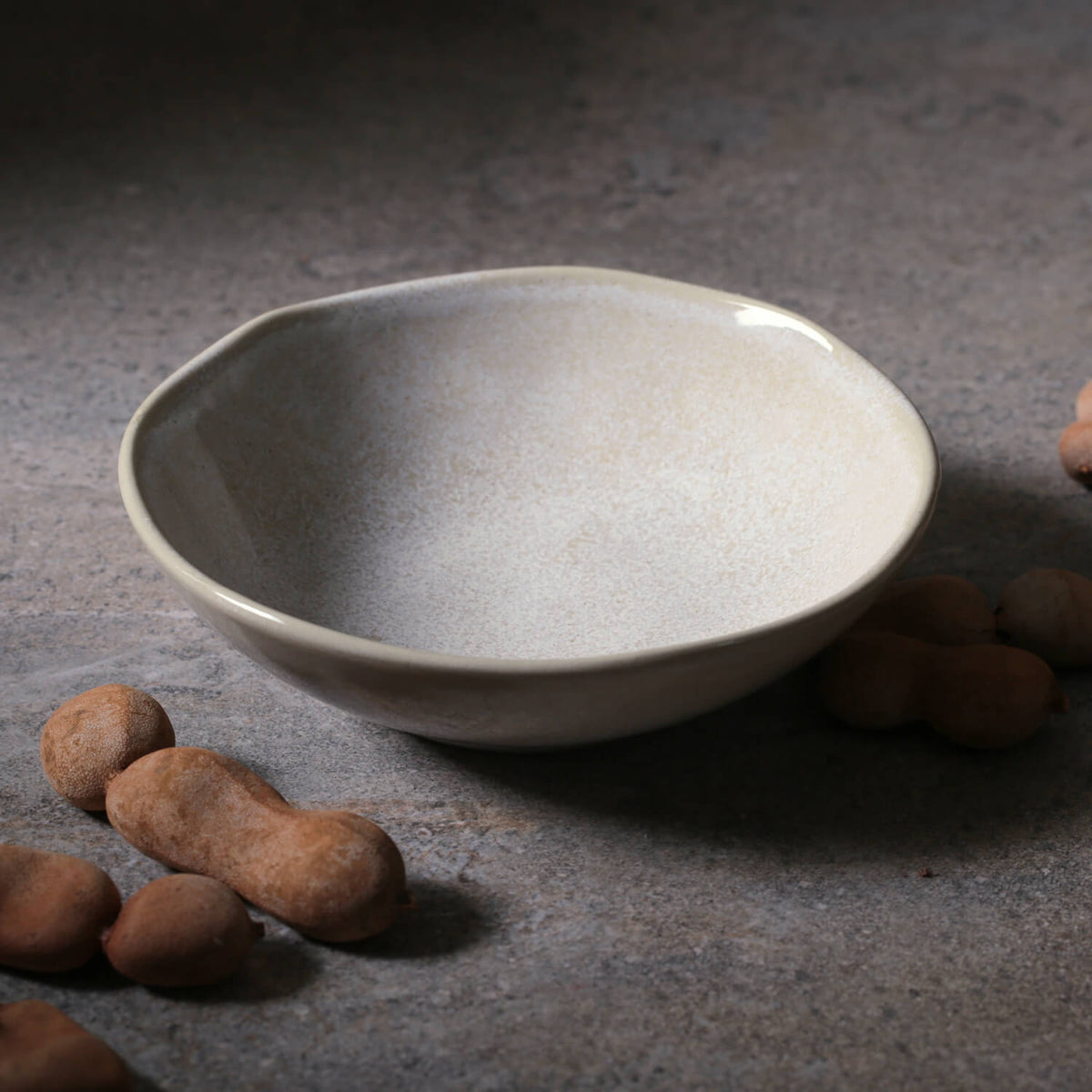 Gray ceramic bowl on a textured surface with brown nut shaped objects.