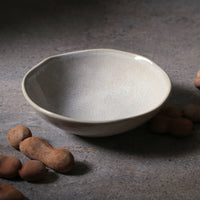 Gray ceramic bowl on a textured surface with brown nut shaped objects.