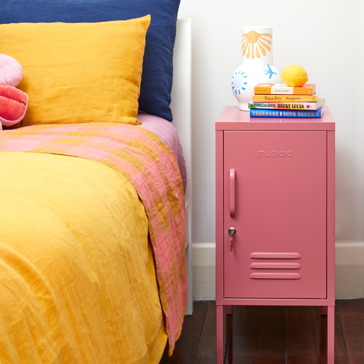 Pink locker-style nightstand next to a bed with colorful bedding