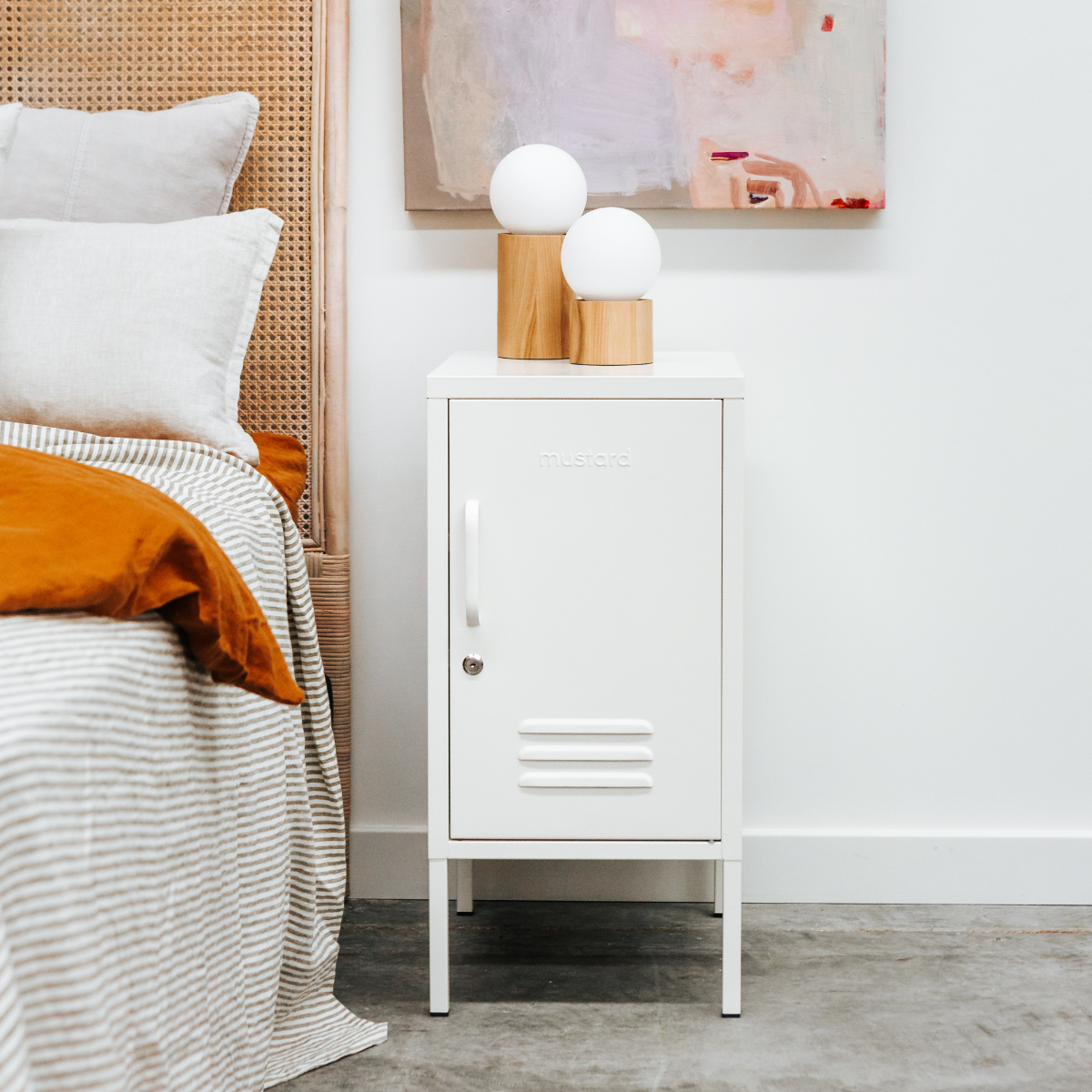 White locker-style nightstand next to a bed with white bedding and orange blanket.