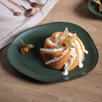 Small bundt cake with white frosting on a green plate on a wooden table.