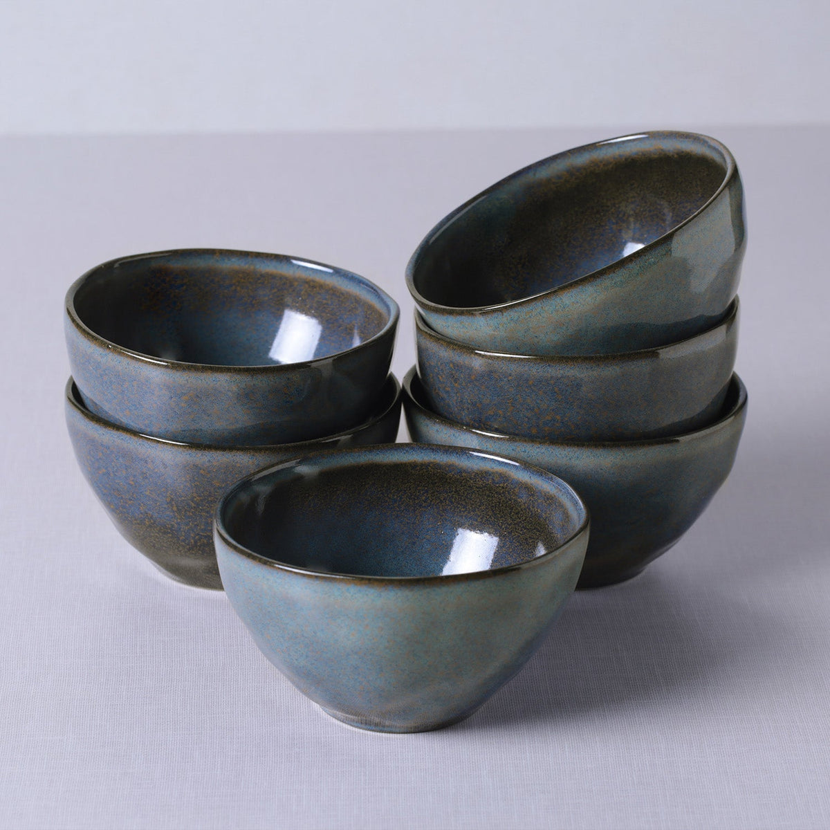 Set of six blue ceramic bowls stacked on a light gray background