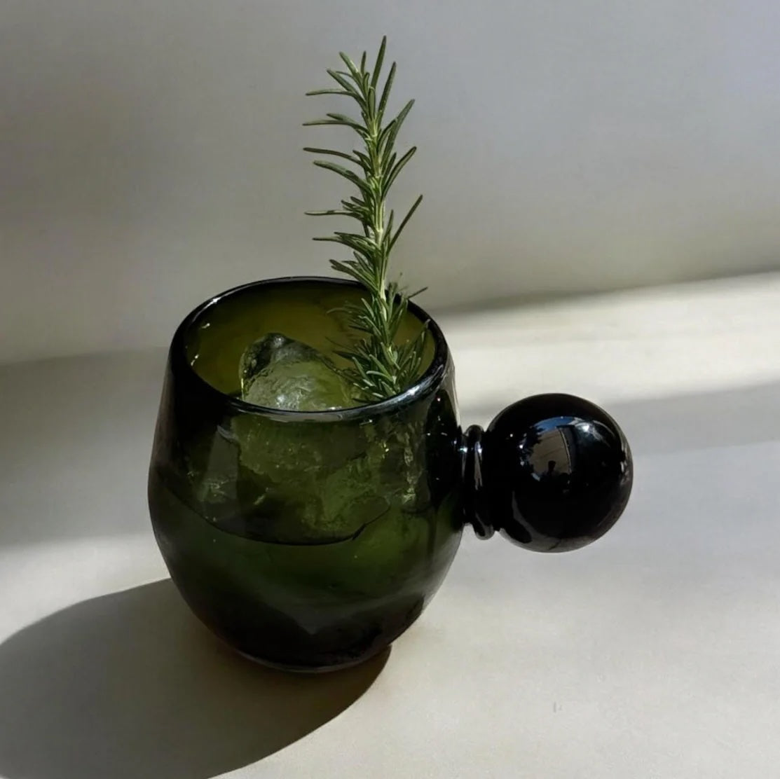 Green glass with ice and rosemary on a white surface