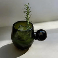 Green glass with ice and rosemary on a white surface