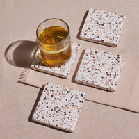 Terrazzo coasters with a glass of amber liquid on a beige surface