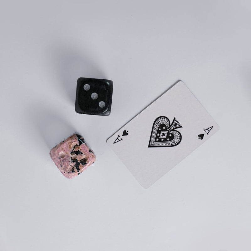 Playing card with a black diamond symbol, two stone dice on a light gray background