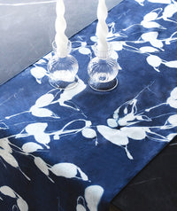 Blue table runner with white floral pattern and glass candle holders on a table.