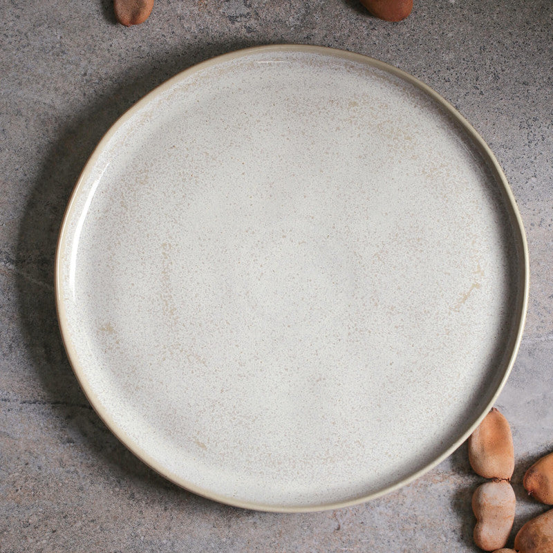 Round beige ceramic plate on a gray surface with small nuts around it