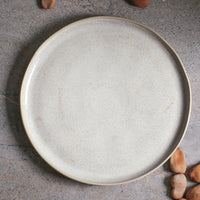 Round beige ceramic plate on a gray surface with small nuts around it